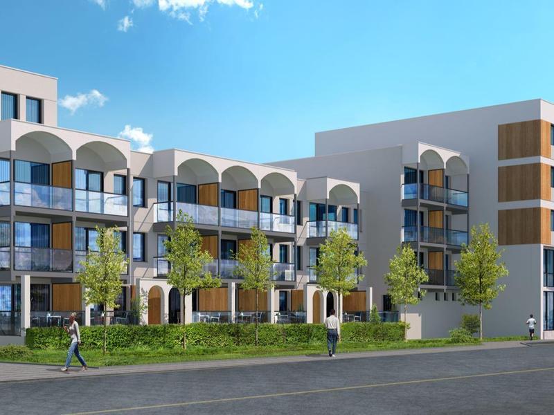 Moderní hotelová budova s balkony, skleněnou fasádou a zelenými stromy pod modrou oblohou.