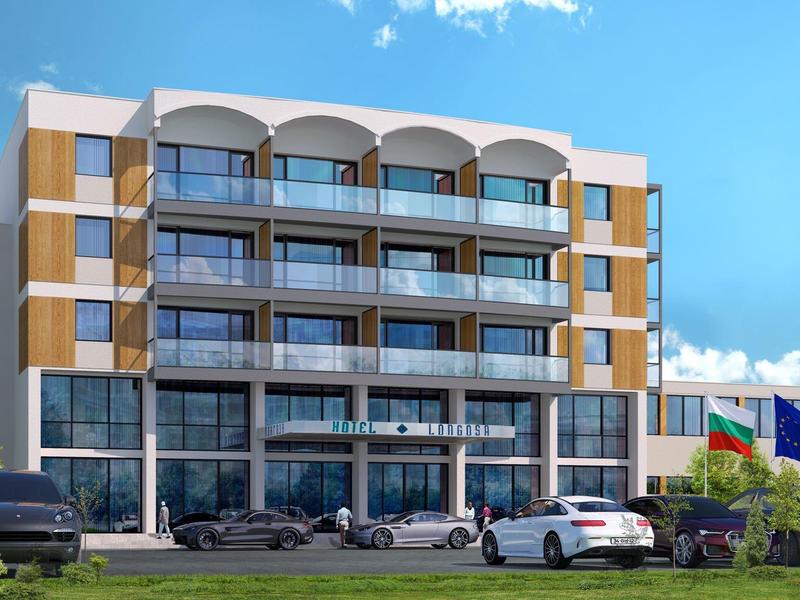 Moderní hotel s několika patry, balkony a zaparkovanými auty před budovou za slunečného počasí.