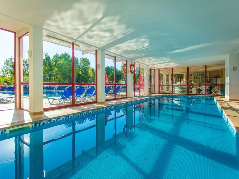Indoor swimming pool with large windows, lounge chairs, and a view of a sunny outdoor area.