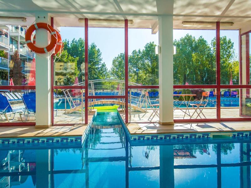 Indoor pool with blue water, red windows, and tables with chairs outside.