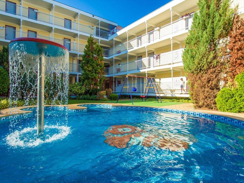 Modern hotel pool with water feature and multi-story building in the background on a sunny day.