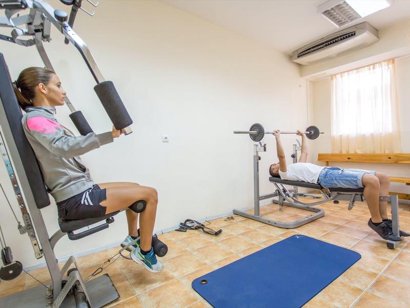 Small gym room with exercise equipment, blue workout mat, and daylight from window.