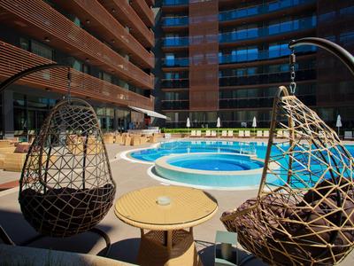 Dziedziniec z okrągłym basenem i dwoma wiszącymi wiklinowymi fotelami przed nowoczesnym hotelem.