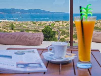 Ein Glas Orangensaft und eine Kaffeetasse auf Tisch mit Meerblick im Hintergrund.