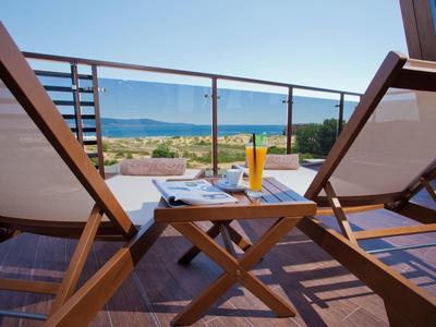 Meerblick von einer Terrasse mit zwei Holzliegen, kleinem Holztisch und erfrischendem Getränk.