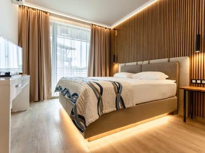 Modernes Schlafzimmer mit großem Bett, Holzlamellenwand, Vorhängen und indirekter Beleuchtung.