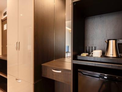 Moderner Küchenbereich mit dunklem Holz, Edelstahl-Wasserkocher, Geschirr und schwarzem Mini-Kühlschrank.