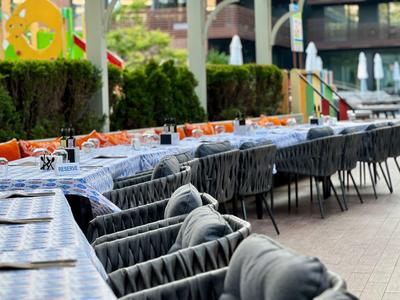 Langgezogener Außenbereich mit gedeckten Tischen und gepolsterten Stühlen in moderner Atmosphäre.