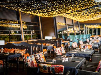 Przytulny taras na zewnątrz z krzesłami i stołami, oświetlony licznymi małymi światłami.