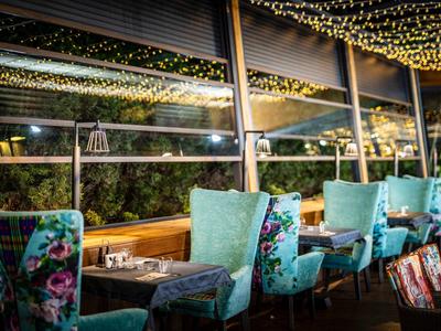 Gemütliche Terrasse mit türkisfarbenen Sesseln, Tischen und warmen Lichterketten an der Decke.