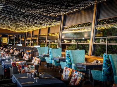 Gemütliches Restaurant mit blauen Sesseln, bunten Kissen und Lichterketten an der Decke.