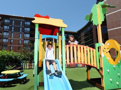 Kinder spielen auf einer farbenfrohen Outdoor-Spielplatzstruktur vor modernen Gebäuden.
