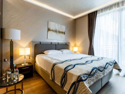 Modernes Hotelzimmer mit Doppelbett, Nachttischen und großen Fenstern mit Vorhängen.