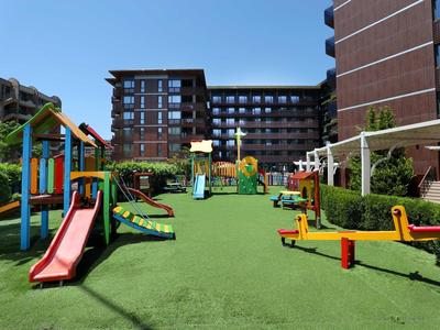 Ein moderner Kinderspielplatz mit Rutschen und Klettergerüsten vor einem Hotelgebäude.