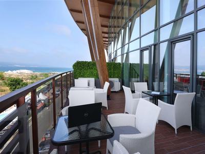 Balkon mit weißen Sesseln und Glastisch mit Meerblick in einem Hotel.