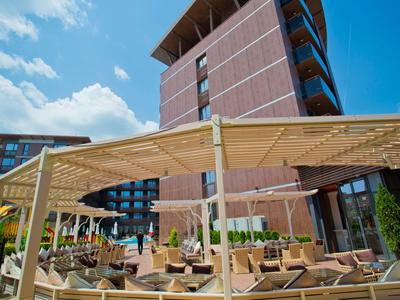 Nowoczesny zewnętrzny obszar hotelu z wygodnymi miejscami do siedzenia i drewnianą pergolą pod niebieskim niebem.