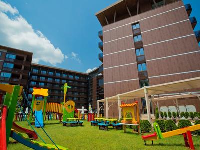 Bunter Kinderspielplatz mit Rutsche und Klettergerüst vor modernen roten Wohngebäuden bei Sonnenschein.
