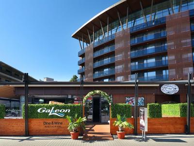 Modernes Hotel mit gebogenem Dach, großen Glasfenstern und einer Terrasse mit Pflanzen und Eingangsbogen.