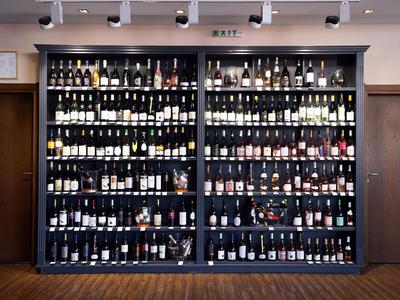 Regalwand mit zahlreichen Weinflaschen verschiedener Farben und Etiketten, Holzfußboden darunter.