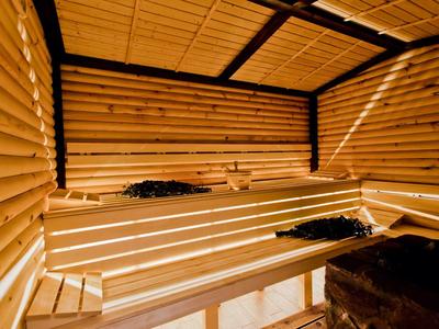 Holzsauna mit mehrstufigen, breiten Holzliegen und dunklem Ofen im rechten Vordergrund.