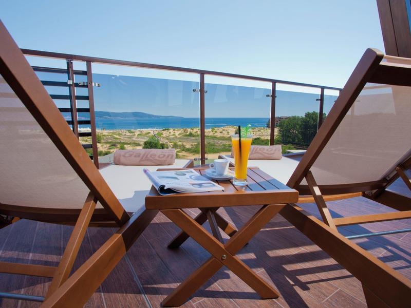 Meerblick von einer Terrasse mit zwei Holzliegen, kleinem Holztisch und erfrischendem Getränk.