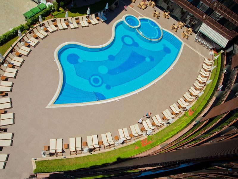 Freizeitbereich mit ungewöhnlichem blauen Pool und vielen weißen Liegestühlen neben einem Gebäude.