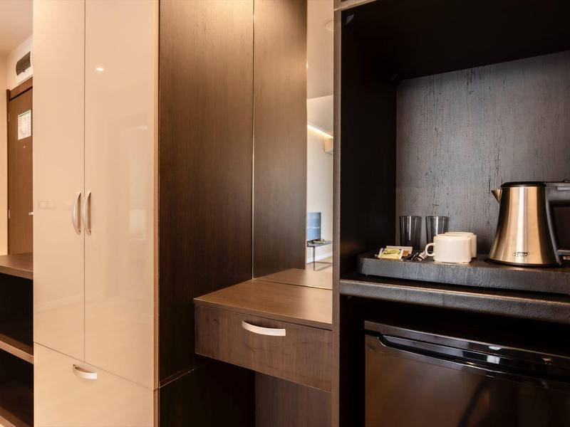 Moderner Küchenbereich mit dunklem Holz, Edelstahl-Wasserkocher, Geschirr und schwarzem Mini-Kühlschrank.