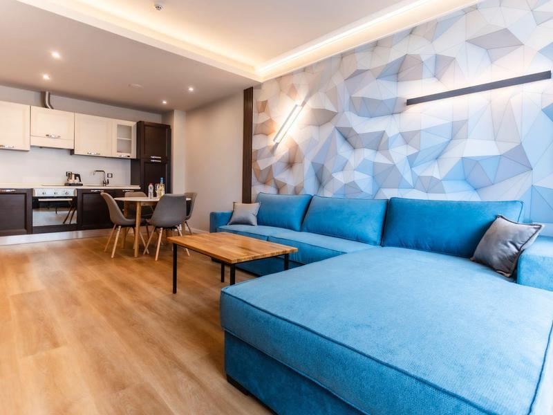 Modern eingerichtetes Hotelzimmer mit blauem Sofa und Küchenzeile im Hintergrund.