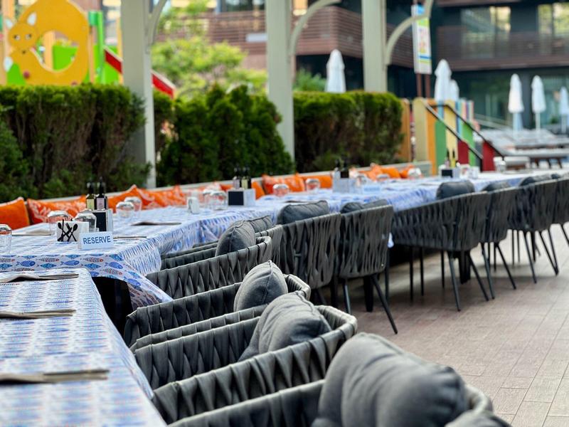 Langgezogener Außenbereich mit gedeckten Tischen und gepolsterten Stühlen in moderner Atmosphäre.