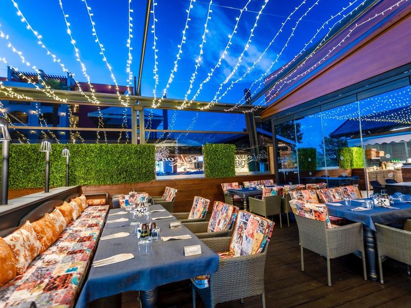 Romantische überdachte Terrasse eines Restaurants mit Lichterketten und gedeckten Tischen