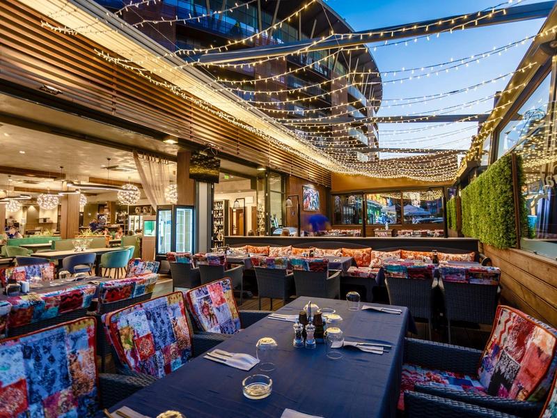 Outdoor-Restaurantbereich mit bunten Sesseln, gedeckten Tischen und Lichterketten am Himmel.