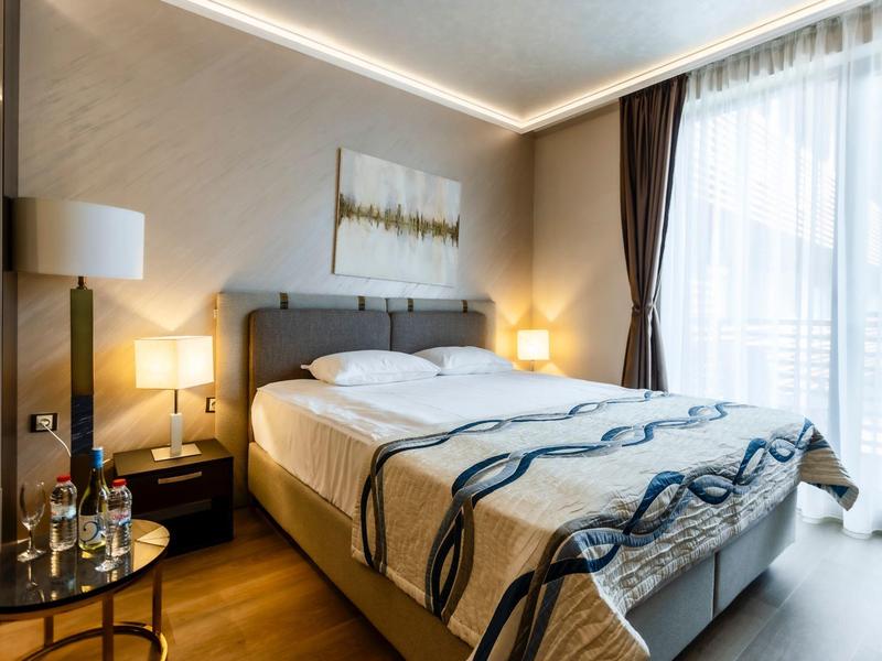 Modernes Hotelzimmer mit Doppelbett, Nachttischen und großen Fenstern mit Vorhängen.