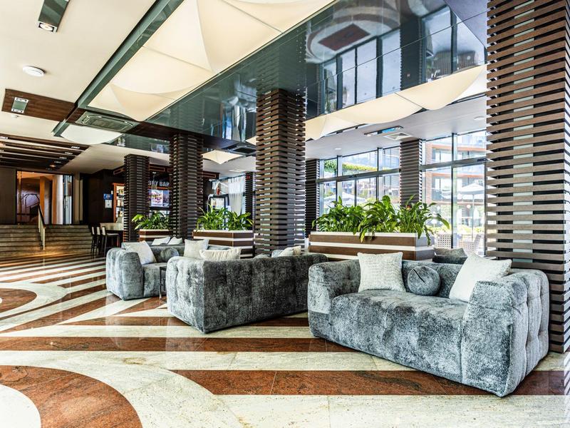 Moderne Hotellobby mit grauen Sofas, Glasdecke und dekorativem Marmorboden.