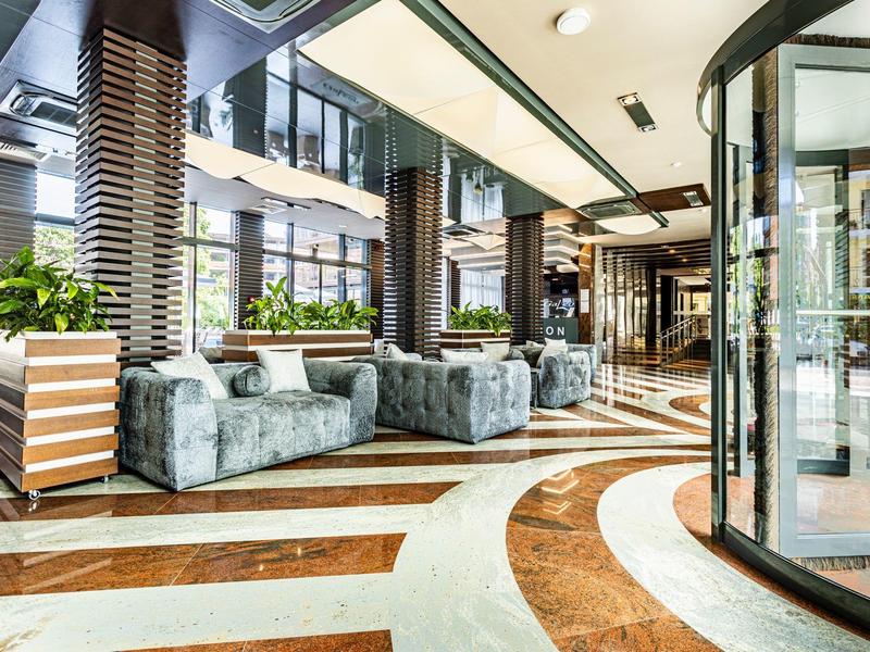Heller Hoteleingangsbereich mit großen Fenstern, Glasdrehtür und bequemen Sitzgelegenheiten.