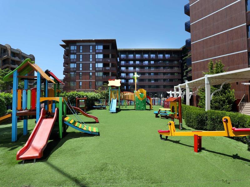 Ein moderner Kinderspielplatz mit Rutschen und Klettergerüsten vor einem Hotelgebäude.