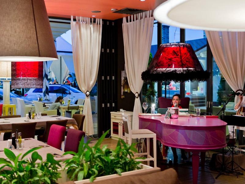 Gemütliches Café mit roten Lampenschirmen, Vorhängen und einem pinkfarbenen Klavier.