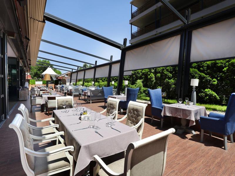 Offene Terrasse mit gedeckten Tischen, bequemen Stühlen und Sonnenschutz auf Holzboden.