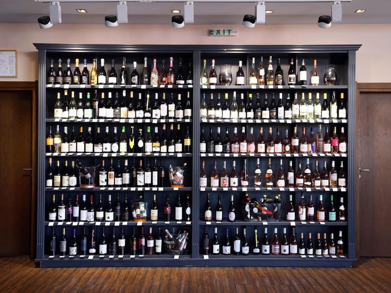 Regalwand mit zahlreichen Weinflaschen verschiedener Farben und Etiketten, Holzfußboden darunter.