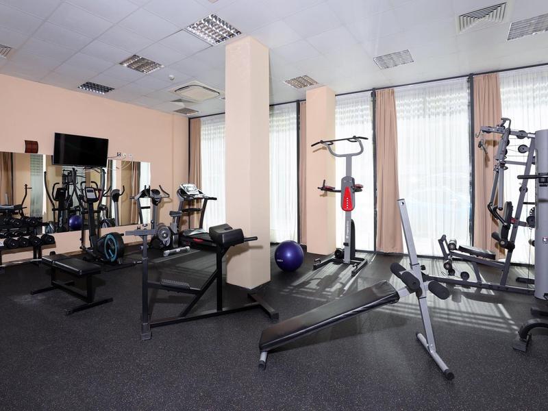 Moderner Fitnessraum mit Hanteln, Laufband, Kraftgerät und Gymnastikball, heller Raum mit Fenstern.