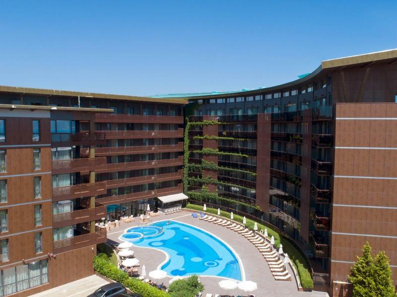 Moderner Hotelkomplex mit großem Außenpool, Liegestühlen und klar blauem Himmel im Hintergrund.