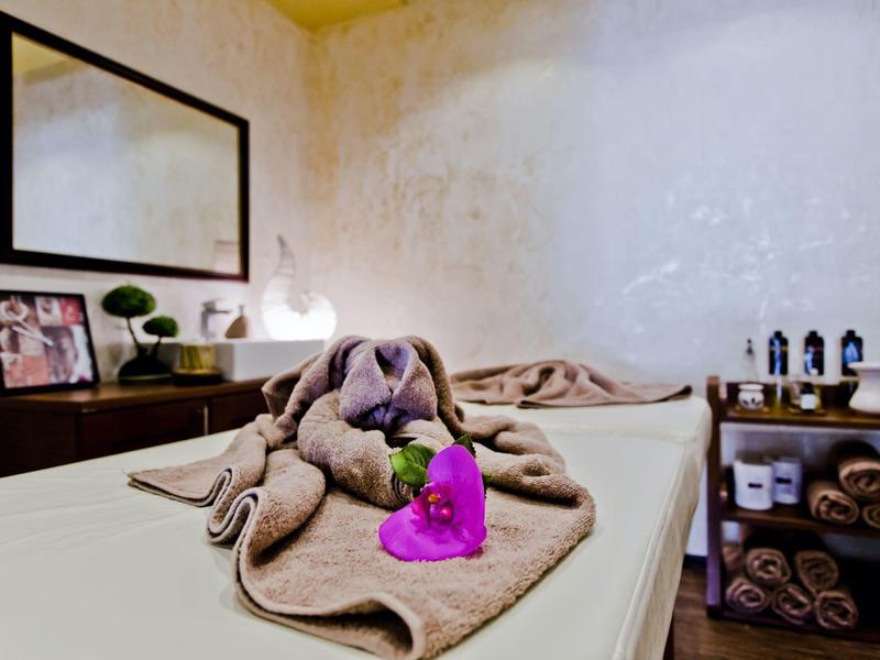 Zimmer mit Massagetisch, Handtüchern, Kuscheltier und entspannender Dekoration in warmen Farben.