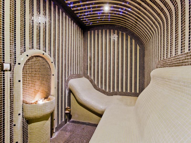 Innenraum einer Sauna mit gerundeten Wänden, gedämpftem Licht und Holzsitzen in Beige und Grau.