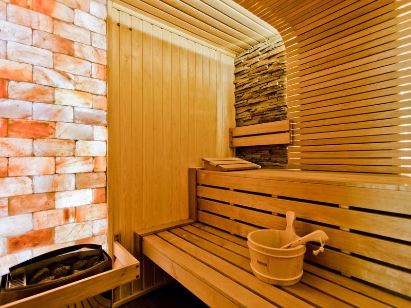 Innenraum einer Sauna mit Holzbank, Holzeimer, Steinwand und Saunaofen mit Steinen.