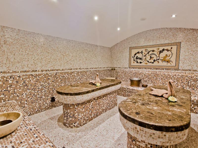 Luxuriöser Mosaik-Dampfraum mit rundem und länglichem Sitzbereich sowie warmem Beleuchtungsakzent.