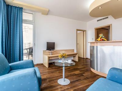 Lichte hotelkamer met blauwe fauteuils, houten vloer, glazen tafel en receptiebalie.