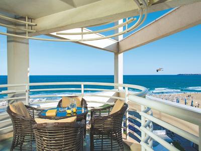 Balkon met eethoek met uitzicht op strand en oceaan onder een helderblauwe hemel.