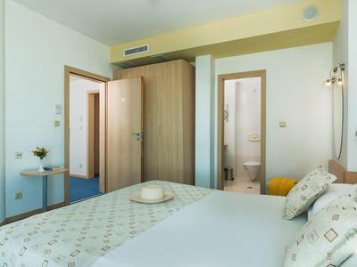 Lichte hotelkamer met tweepersoonsbed, houten deuren, klein rond tafeltje en ingang naar badkamer.