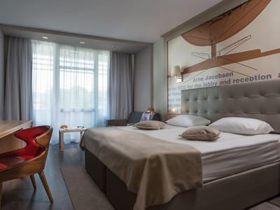 Moderne hotelkamer met een groot bed, bureau met stoel en raam met doorschijnende gordijnen.