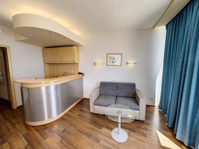 Moderne hotellobby met gebogen receptiebalie, grijze bank, witte tafel, houten vloer en blauwe gordijnen.