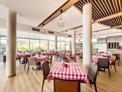 Lichte hotel eetzaal met geruite tafelkleden, houten plafond en grote ramen.
